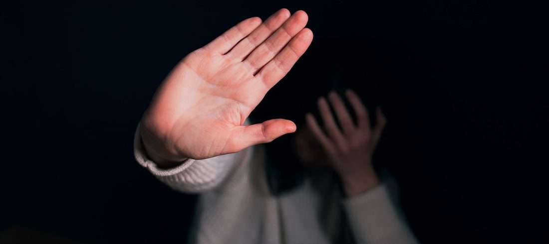 An image of a person holding their hand in front of their face and putting up their hand in a stop motion, an image paired with a blog on domestic violence