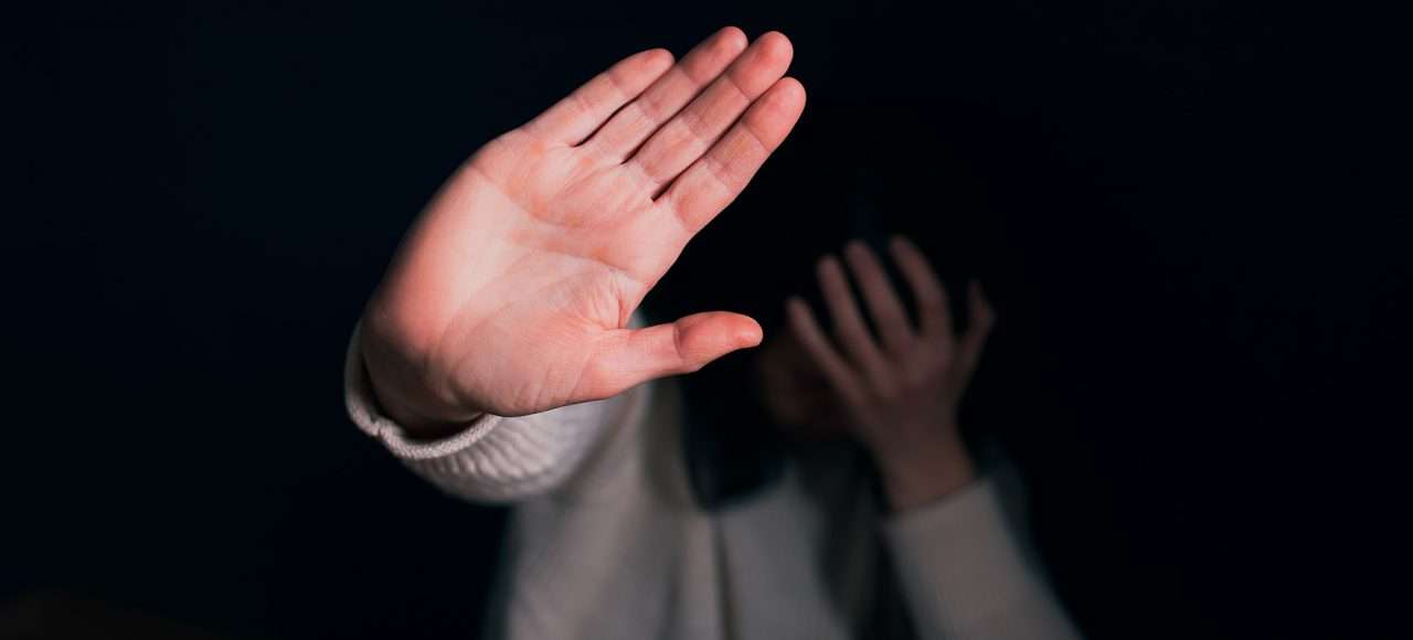 An image of a person holding their hand in front of their face and putting up their hand in a stop motion, an image paired with a blog on domestic violence