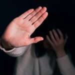 An image of a person holding their hand in front of their face and putting up their hand in a stop motion, an image paired with a blog on domestic violence