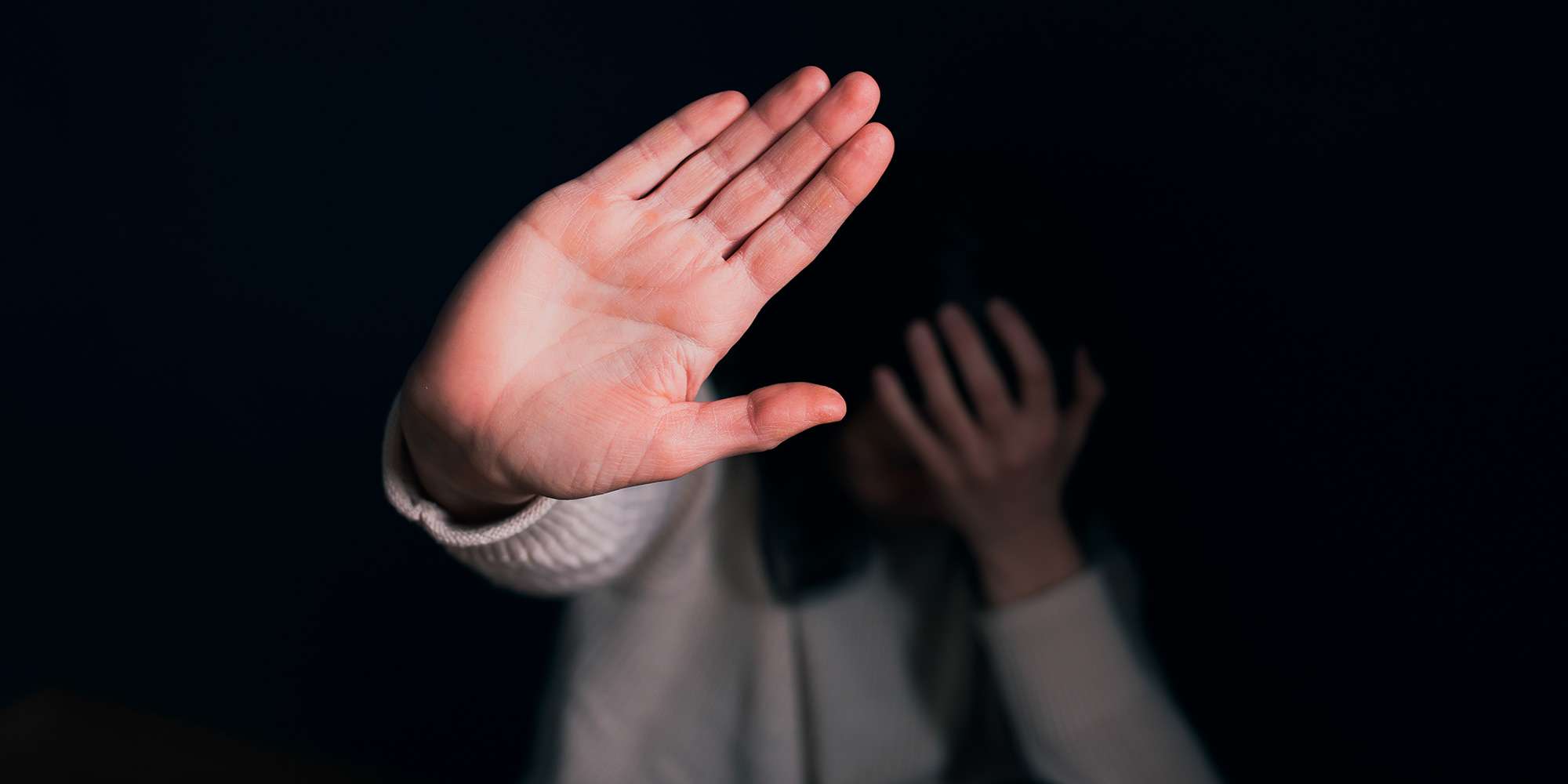 An image of a person holding their hand in front of their face and putting up their hand in a stop motion, an image paired with a blog on domestic violence