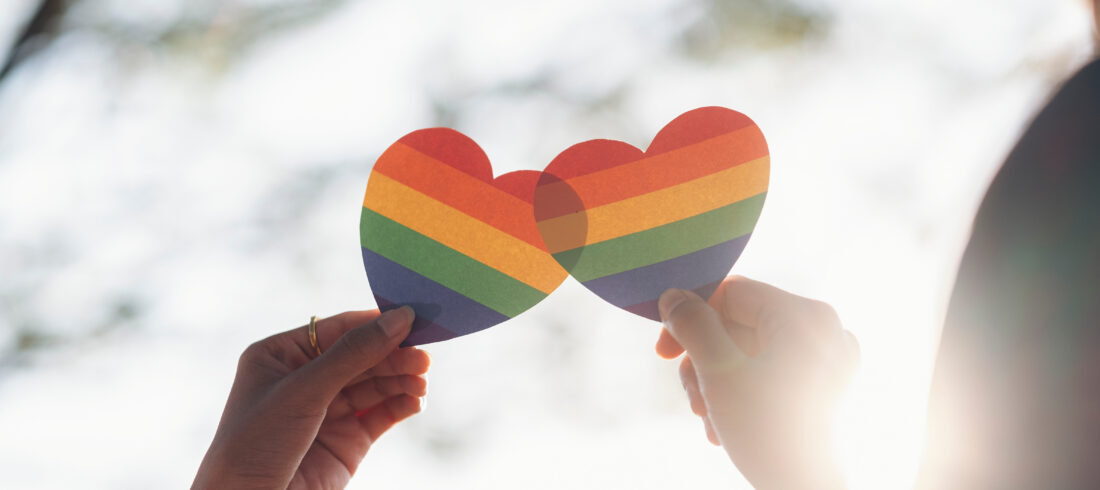 Close up hand of LGBTQ couple holding rainbow heart.