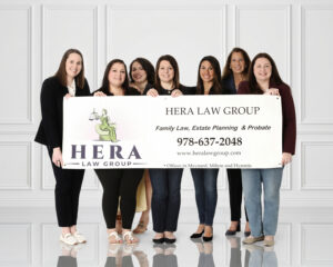 Hera Law Group standing together holding a firm banner listing family law, estate planning, and probate services, with offices in Maynard, Milton, Cumberland, and Hyannis.